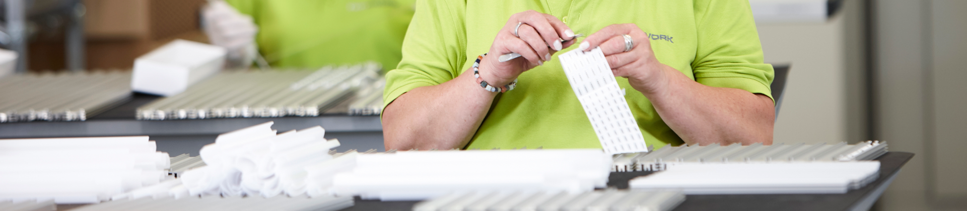 Mitarbeiterinnen in grüner Arbeitskleidung bei der manuellen Konfektionierung von LED-Komponenten an einem Montagplatz – präzise Handarbeit in der Produktion.